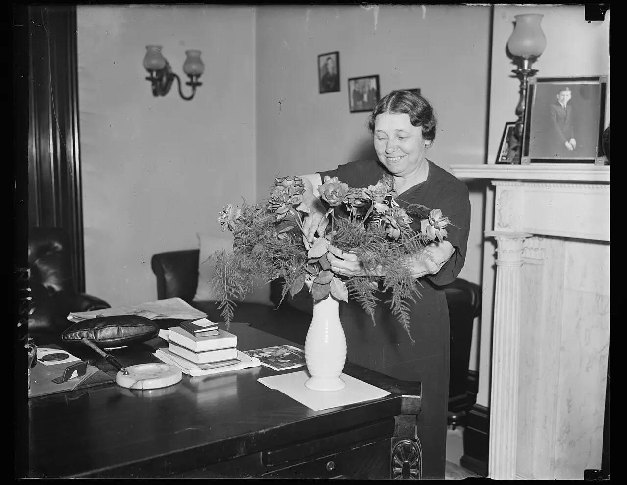 A 1936 photograph of Senator Hattie Caraway smiling in her office as she arranges a vase of flowers.