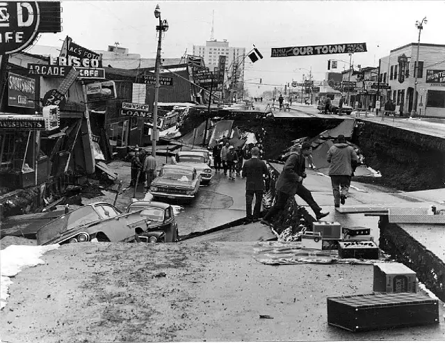 Fourth Avenue in Anchorage, Alaska, after the 1964 earthquake: collapsed roadway, tilted and damaged buildings, and cars stranded in the rubble.
