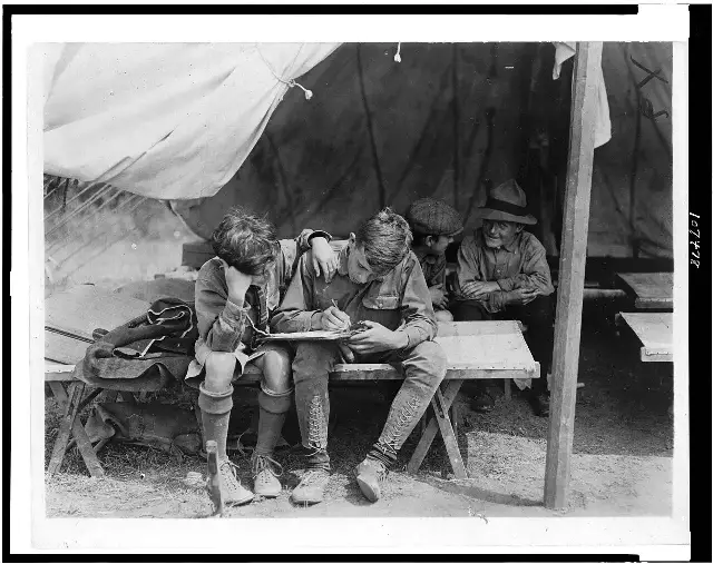 Four Boy Scouts at a 1912 camp on Hunter's Island write letters home from inside a tent
