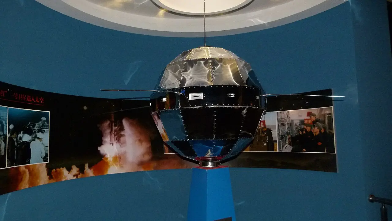 A museum model of the Dong Fang Hong 1 satellite: a faceted metal sphere about a meter across with four long whip antennas.