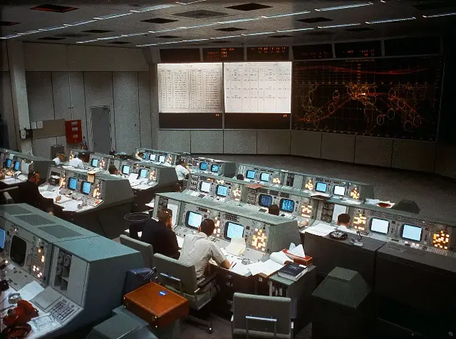 NASA's Mission Control room in Houston during the Gemini 7 spaceflight in December 1965, with flight controllers at consoles beneath large trajectory display boards
