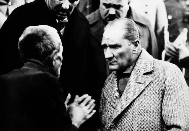 Mustafa Kemal Atatürk standing on a balcony in Tokat in 1930, in civilian dress and hat, listening intently to an elderly citizen below him