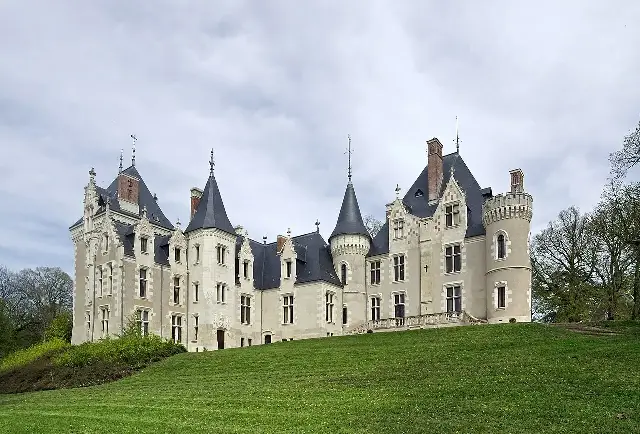 The Chateau de Cande, a stone French chateau with slate roofs and turrets, photographed on a grassy hill in Monts, France.
