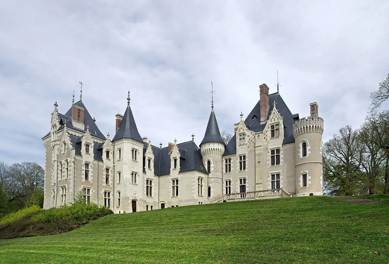 The Chateau de Cande, a stone French chateau with slate roofs and turrets, photographed on a grassy hill in Monts, France.