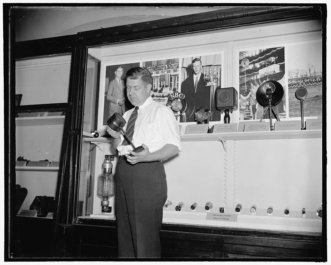 A 1938 photograph of a man holding the 'Tomato Can' microphone that carried KDKA's first 1920 broadcast, on display in a Smithsonian exhibit case.