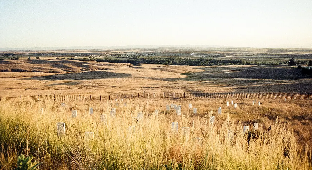 Rolling golden grassland of the Little Bighorn battlefield in Montana, with white markers scattered across the field where soldiers fell.