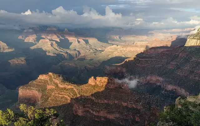 The Grand Canyon's layered red rock formations glowing in evening light under dramatic clouds, viewed from Powell Point.