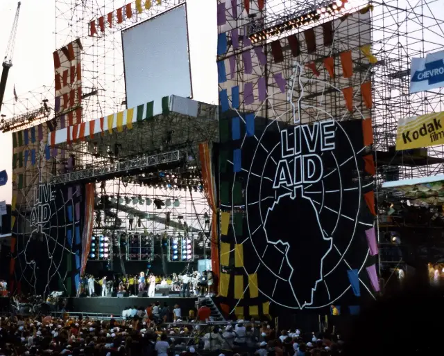 The Live Aid stage at JFK Stadium in Philadelphia, July 13, 1985, with the iconic Live Aid banner and a large crowd.