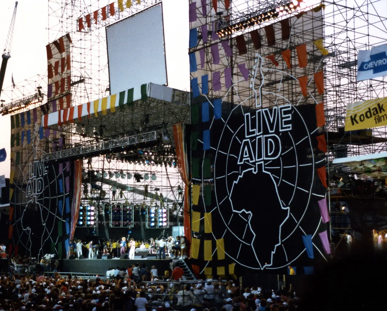 The Live Aid stage at JFK Stadium in Philadelphia, July 13, 1985, with the iconic Live Aid banner and a large crowd.