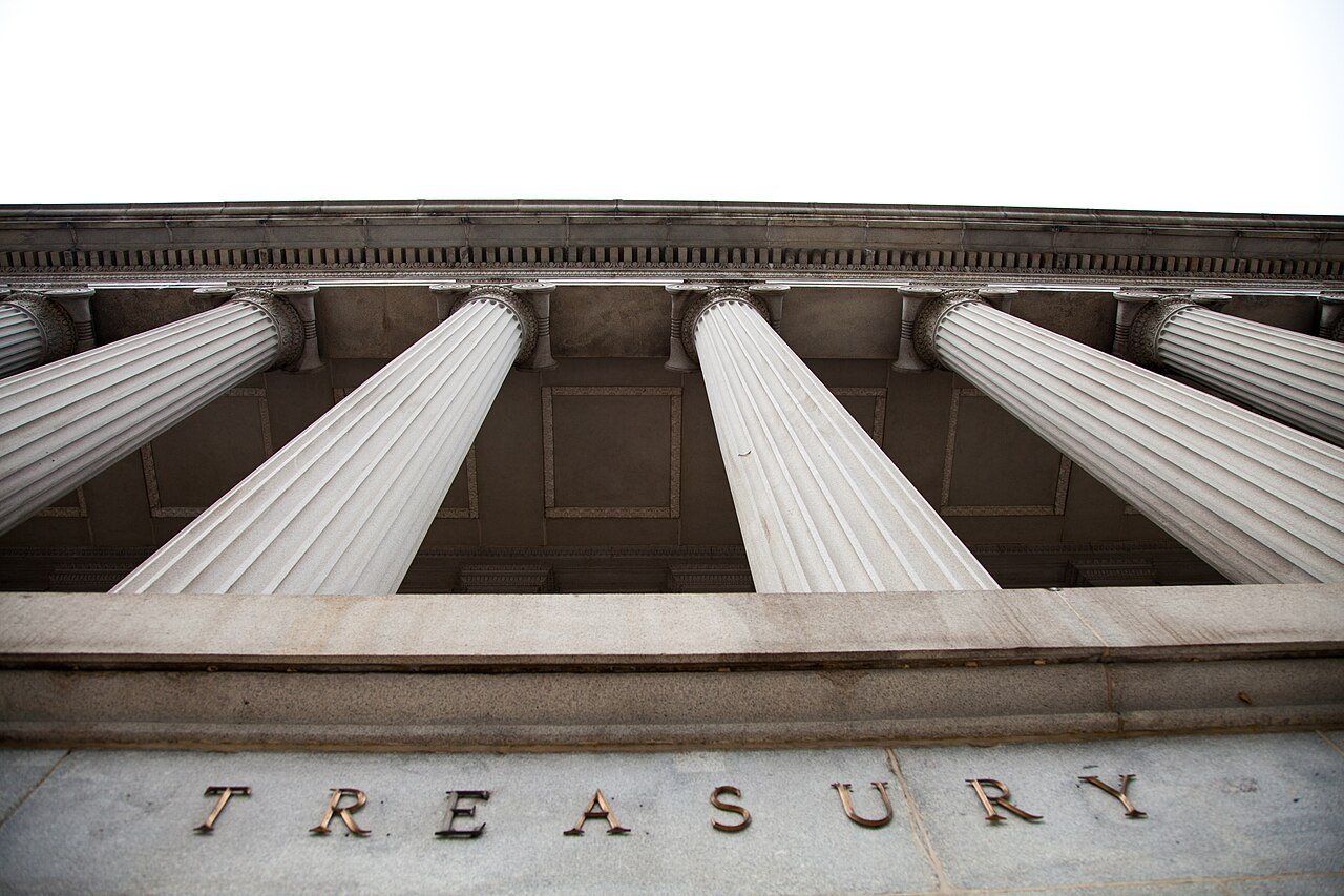 Looking up at the stone columns and TREASURY lettering of the U.S. Treasury Department building in Washington, D.C.