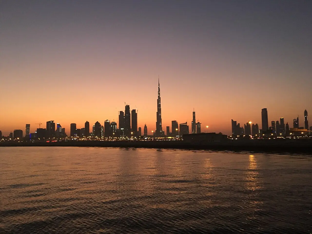 The Burj Khalifa rising over the Dubai skyline at sunset, seen from across the water.
