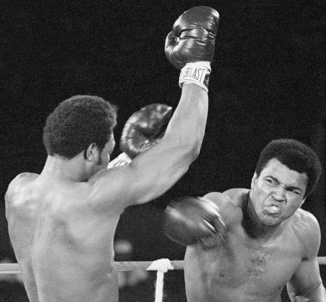 Black-and-white fight photograph from the Rumble in the Jungle showing Muhammad Ali landing a right hand to George Foreman's face in the ring