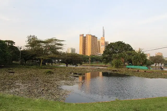 A lake at Uhuru Park in Nairobi at sunset, with the Nairobi skyline reflected in the water.