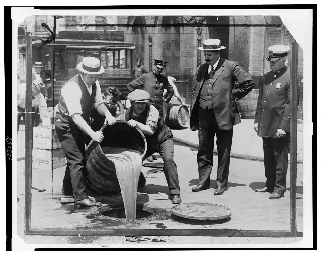 Prohibition agents pouring seized liquor into a New York City sewer while Deputy Police Commissioner John A. Leach watches, during the height of Prohibition.