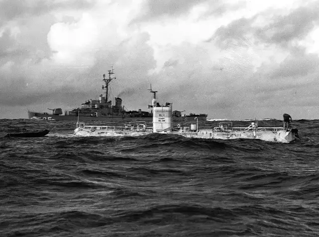 A 1960 U.S. Navy photograph showing the bathyscaphe Trieste floating on the rough ocean surface with the escort ship USS Lewis behind it, on the morning of the Challenger Deep dive.