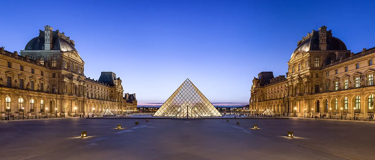 The Louvre courtyard in Paris at dusk, with the glass pyramid glowing in the center.
