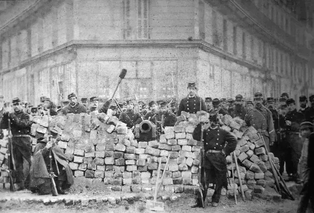 An 1871 photograph of a Paris Commune barricade built of paving stones, with armed National Guardsmen and a cannon behind it.