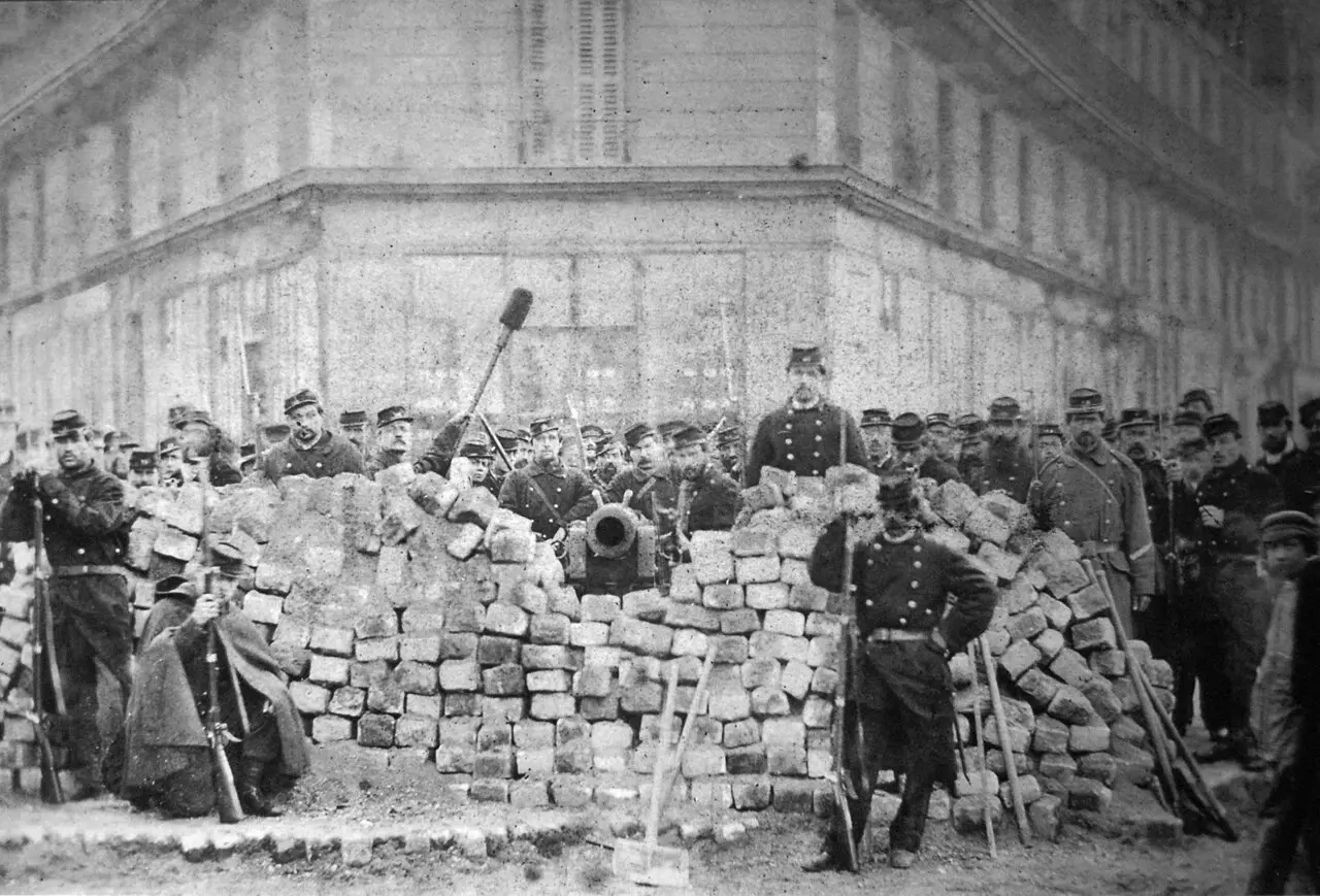 An 1871 photograph of a Paris Commune barricade built of paving stones, with armed National Guardsmen and a cannon behind it.