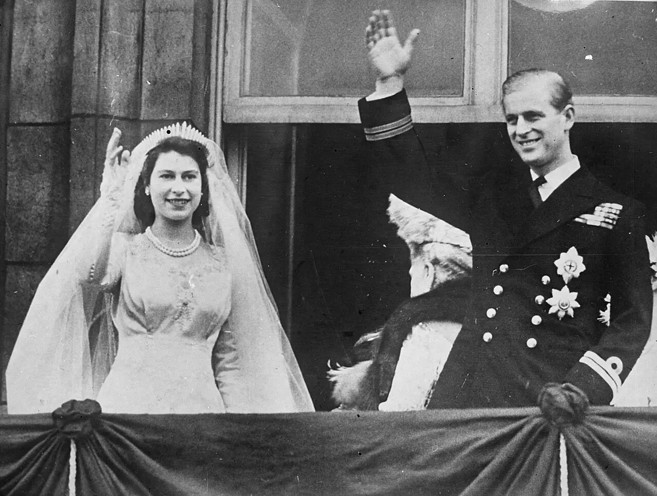 Princess Elizabeth, wearing her Norman Hartnell wedding gown and tiara, waves beside Lieutenant Philip Mountbatten in naval uniform from the Buckingham Palace balcony on their wedding day, November 20, 1947.