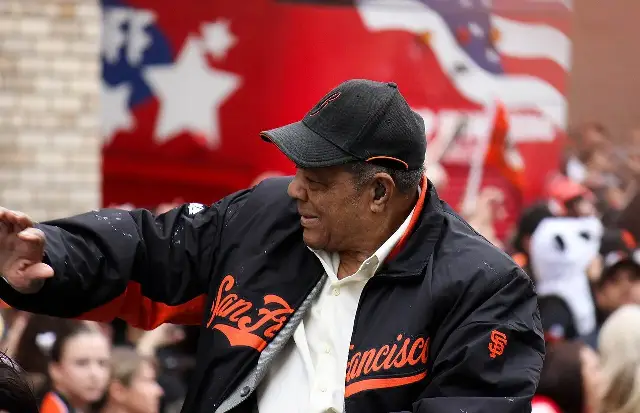 Willie Mays in a San Francisco Giants jacket waving to fans at a parade