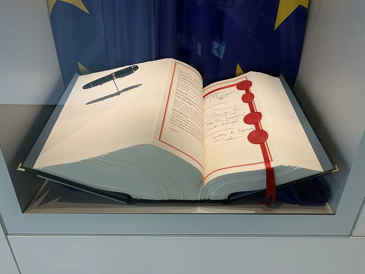 An open display copy of the Maastricht Treaty with signatures and red seals, shown in a museum exhibit with the EU flag — an illustration of the treaty document, not the 1993 signing.
