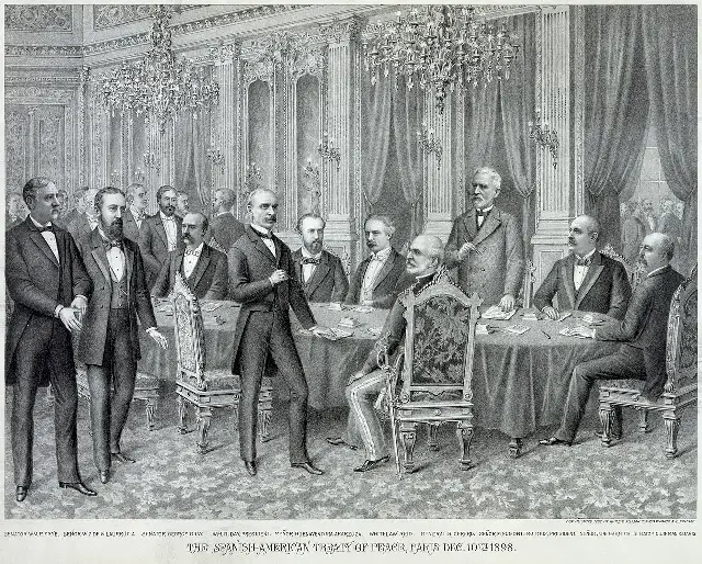 1898 chromolithograph of the signing of the Treaty of Paris, showing American and Spanish commissioners around a table.
