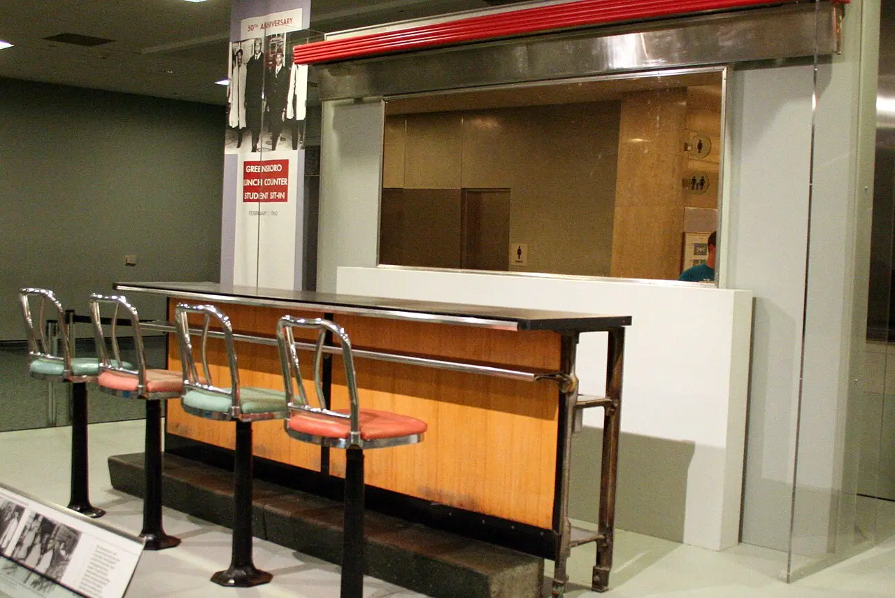 The preserved Greensboro Woolworth's lunch counter on display at the Smithsonian National Museum of American History, with a banner marking the February 1960 student sit-in.