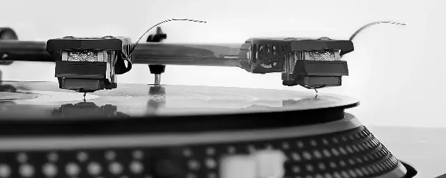 A close-up of a turntable tonearm with its stylus resting on a spinning vinyl record.